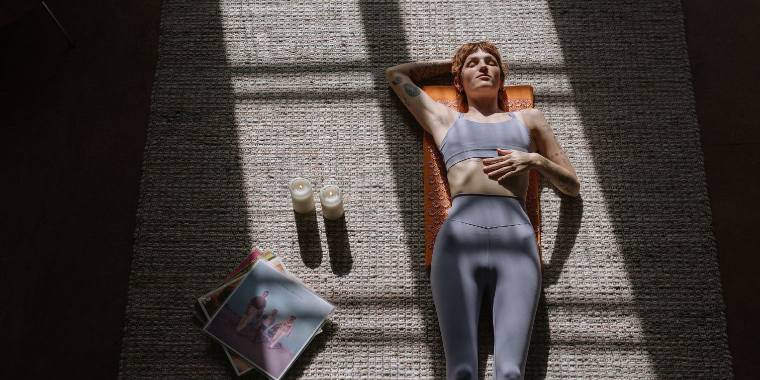 Woman laying on a Shakti Acupressure Mat on beige carpet